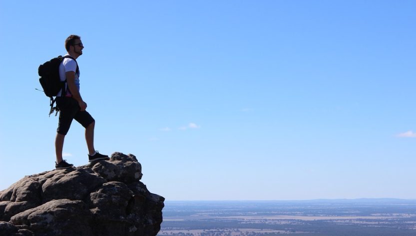 Hombre mirando desde las alturas al horizonte luego de realizar senderismo por la naturaleza.