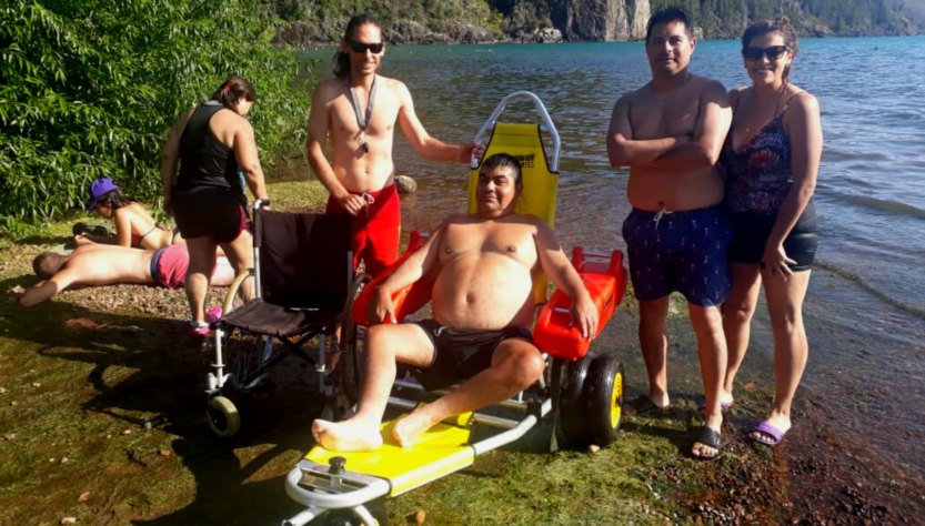 Personas en el Lago Puelo asistiendo a un hombre en la silla anfibia.