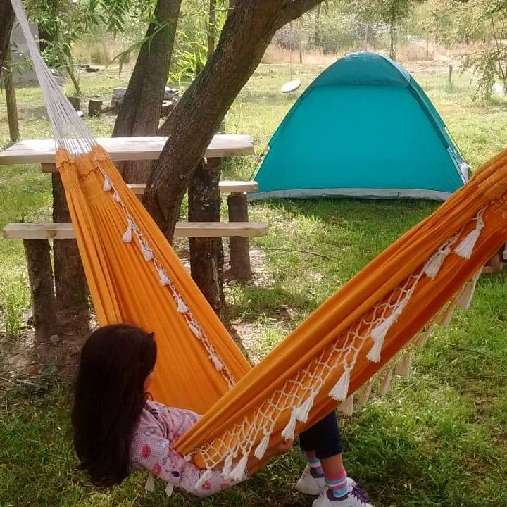 Mujer en una hamaca con una carpa detrás. Camping Frodo en El Bolsón.