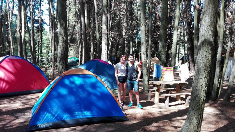 Pareja en medio del bosque con carpas en el camping La Chacra de El Bolsón.